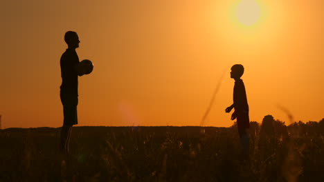Father-and-son-playing-football-in-the-park-at-sunset-silhouettes-against-the-backdrop-of-a-bright-sun-slow-motion-shooting.
